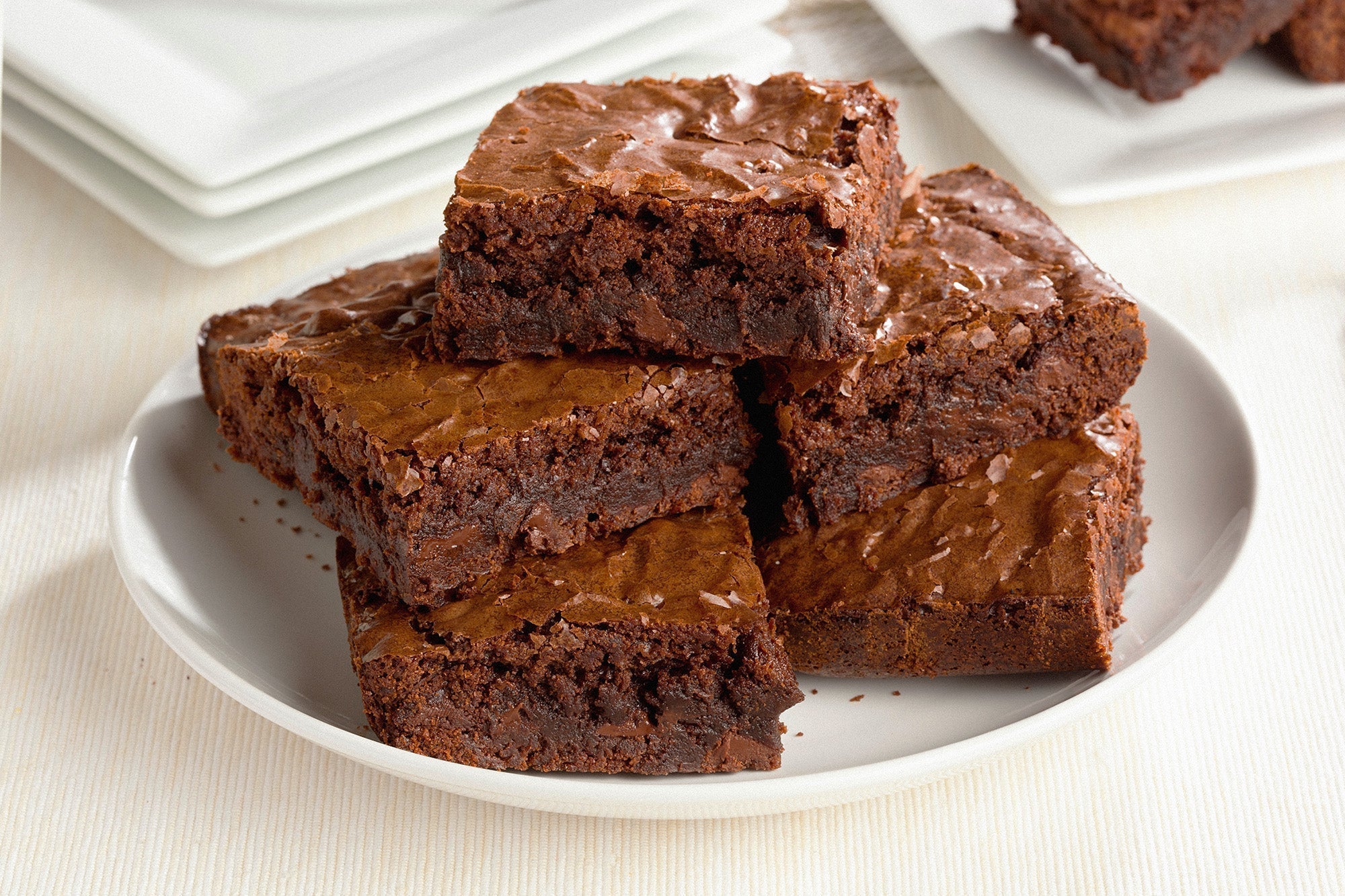 Stack of rich, fudgy chocolate brownies with a shiny, crackled top on a white plate.