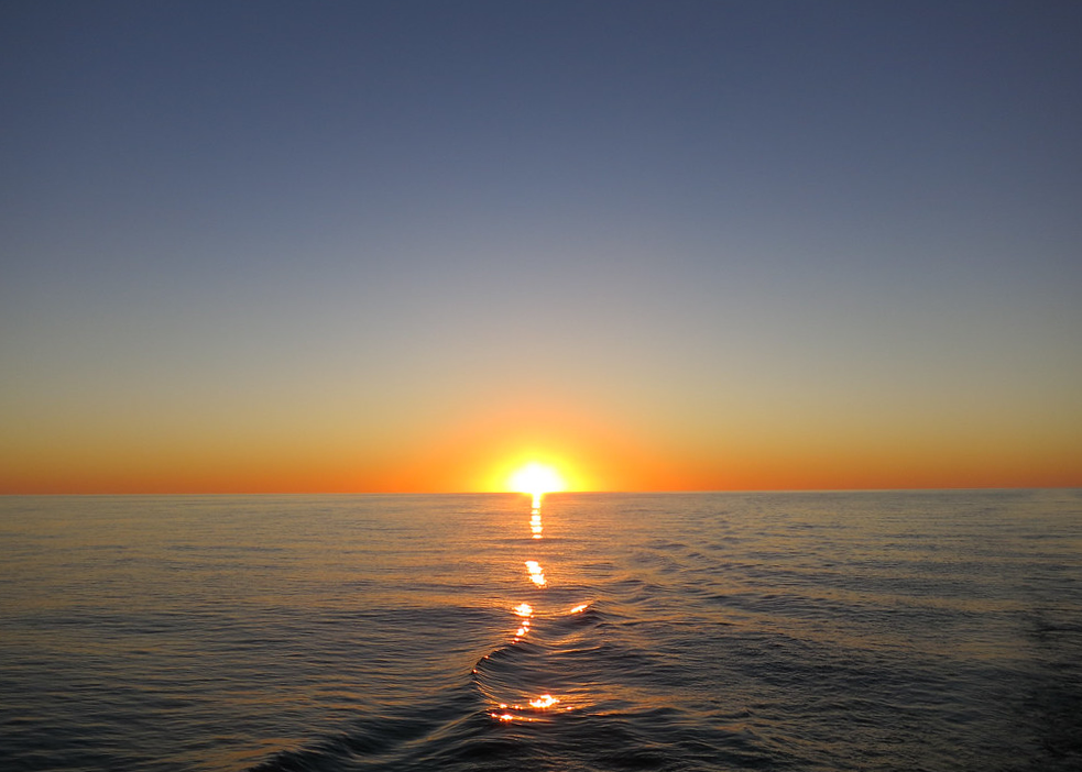 Sunset over calm ocean waters, with golden light reflecting in a straight path toward the viewer.