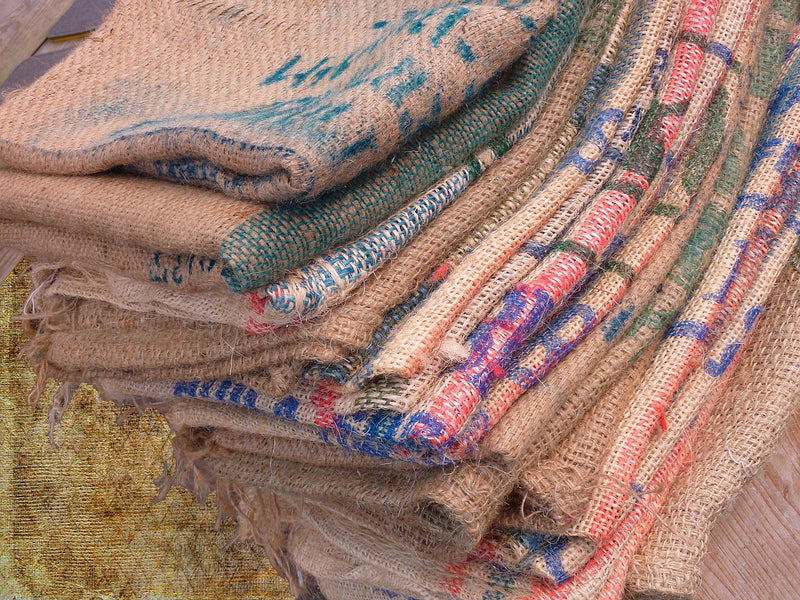 Stack of folded burlap coffee sacks with colorful stitching and printed markings.