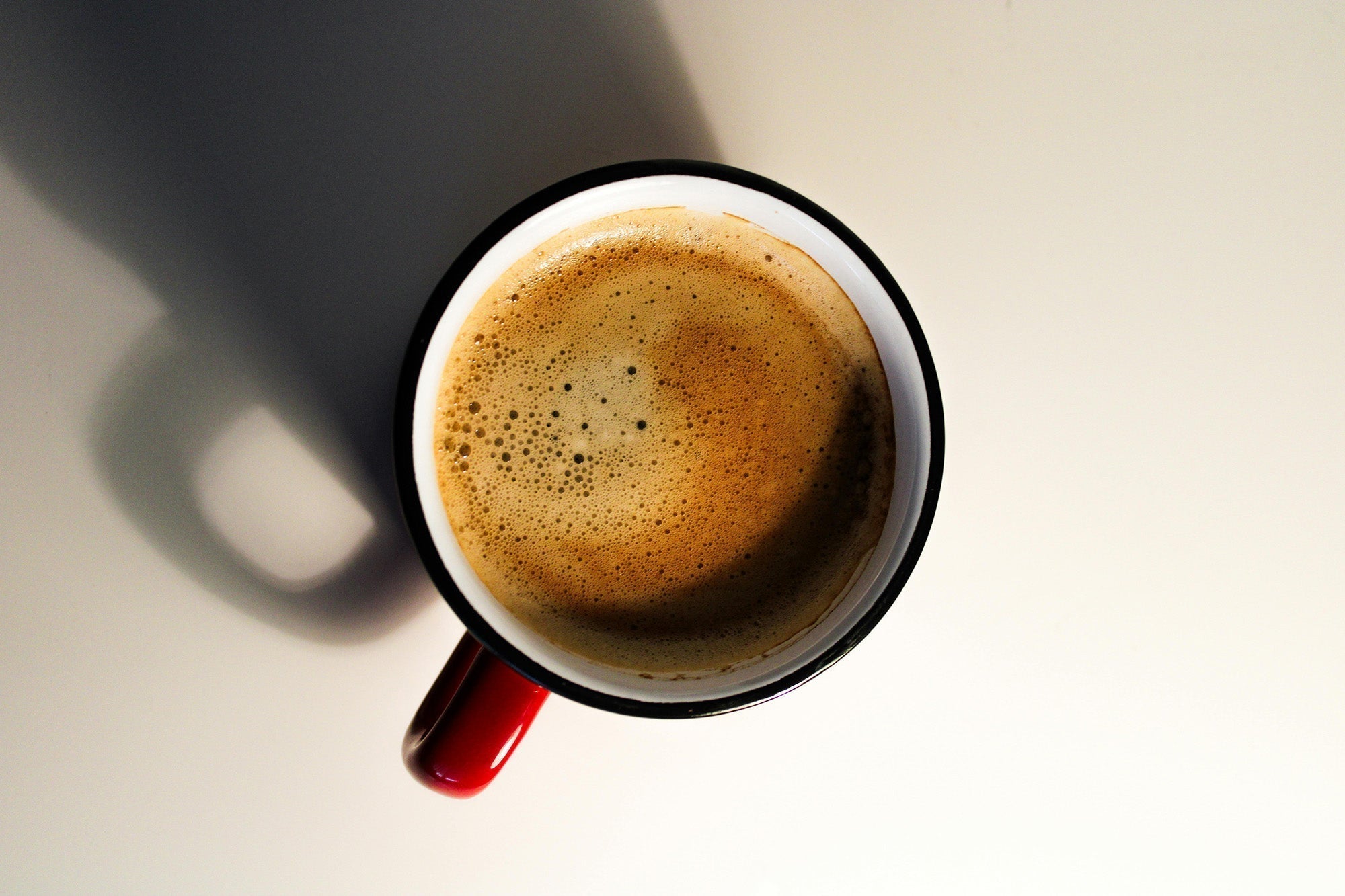 Frothy coffee in a red-handled mug on a plain background.